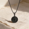 Black stainless steel compass pendant resting on Jerusalem stone