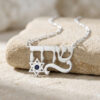 Sterling silver Hebrew name necklace with Star of David and blue birthstone resting on light stone