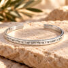 Sterling silver engraved cuff bracelet with a Hebrew blessing resting on a travertine stone block