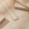 Sterling silver tiny Hebrew name necklace laid on a beige stone, small 8mm Hebrew name jewelry