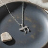 Sterling silver cubic zirconia Chai pendant on a dark ceramic plate beside a small stone