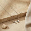 Sterling silver tiny Hebrew name necklace on a stone block with soft fabric, everyday Hebrew name pendant