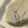 Nano Bible necklace draped over a smooth round stone, showing the 23mm silver Priestly Blessing disc