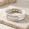 White braided leather bracelet with a silver stainless steel nameplate on travertine stone, engraved name bracelet