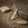 Sterling silver Custom Hebrew Name Necklace with a vertical Hebrew name pendant reading Ahava (אהבה), Hebrew for love on sand beside a stone and dried grass
