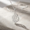 Sterling silver Hebrew flame pendant casting a shadow on a stone surface