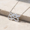 Sterling silver Custom Hebrew Name Necklace resting on stone, hand engraved Hebrew name pendant with heart and swirl