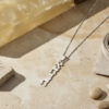 Sterling silver Custom Hebrew Name Necklace, Hebrew name pendant reading Ahava (אהבה), Hebrew for love with silver chain lying on a marble surface with pebbles