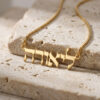 Gold plated tiny Hebrew name necklace on a stone block in warm light, close-up of the Hebrew letters