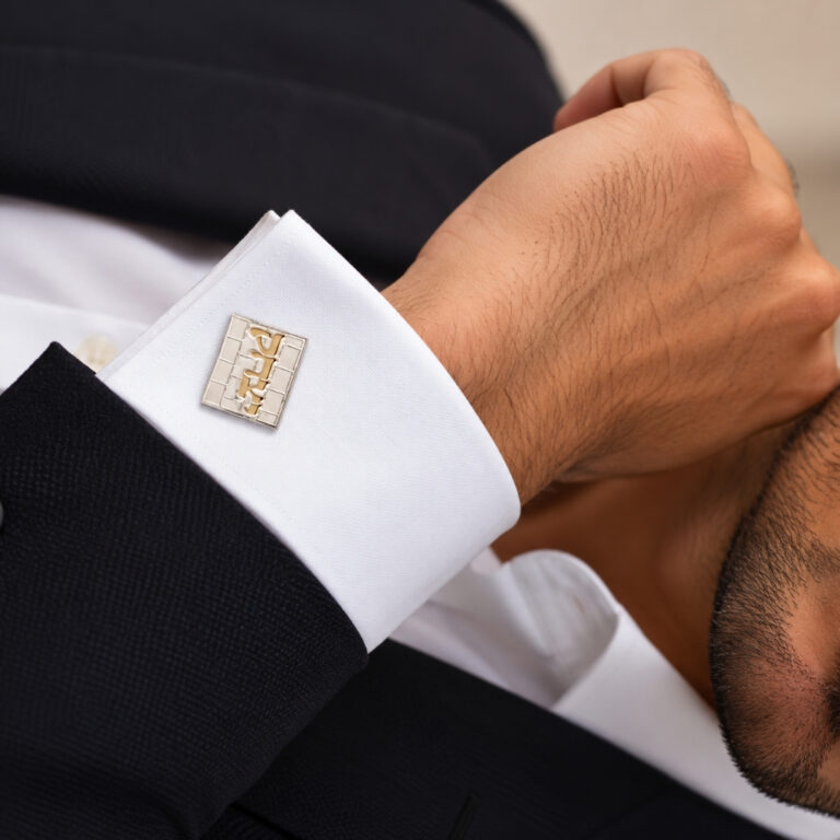 Man in a black suit wearing personalized Hebrew name Kotel cufflinks with a gold name on a white French cuff shirt