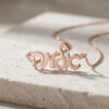 Rose gold plated custom Hebrew script name necklace resting on travertine stone