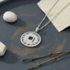 Silver Nano Bible necklace on dark slate with a white pebble and dried twigs, Hebrew Priestly Blessing engraving