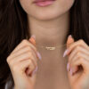 Woman holding the chain of her tiny gold Hebrew name necklace, showing the small pendant size on the neck