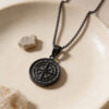 Black stainless steel compass pendant resting in a stone dish