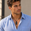 Man in a light blue shirt wearing the black dog tag necklace for men, a Hebrew engraved stainless steel pendant on a curb chain