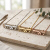 Tiny Hebrew name necklaces in silver, gold and rose gold plated finishes displayed together on a stone block
