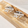 Sterling silver cufflinks with the same Hebrew name cut out on both, displayed on an olive wood board