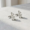 Side view of sterling silver Hebrew name cufflinks with cutout letters standing on a light stone surface
