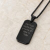 Matte black dog tag pendant with Star of David and Hebrew verse, angled on beige travertine to show the engraving