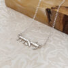 Sterling silver tiny Hebrew name necklace on a textured stone surface, minimalist Hebrew pendant