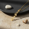 24K gold plated Custom Hebrew Name Necklace lying on sand beside a black plate and pebbles, Hebrew name pendant reading Juliet (ג'ולייט) with gold chain