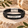 Black braided leather bracelet engraved Always With You in English script, on stone with olive leaves