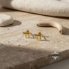 24K Gold Plated Chai earrings on light travertine slab with neutral linen drape, premium Judaica gift presentation