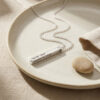 Silver 3D bar necklace with Hebrew engraving on a beige ceramic plate
