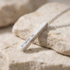 Hammered sterling silver 3D bar necklace engraved in Hebrew resting on stone