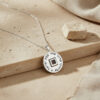 Silver round Shema Yisrael pendant hanging over a travertine stone ledge