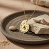 24K gold plated Shema Yisrael nano Bible necklace on a dark stone tray with sand and pebble