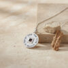 Sterling silver Shema Yisrael nano Bible necklace lying on sand beside stones and driftwood