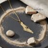 Gold map of Israel pendant on dark sand with stones