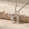 Sterling silver open outline Hebrew Chai necklace resting on a travertine stone block