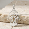925 sterling silver openwork Hamsa pendant with evil eye on a box chain, resting on travertine stone