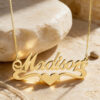 14K yellow gold script name necklace with a heart, resting on a cream travertine stone