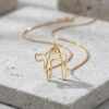 Gold open outline Hebrew Chai pendant on a fine chain, resting on gray stone