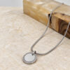 Silver zircon halo pendant on a snake chain beside olive wood