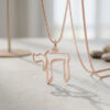 Rose gold open outline Chai necklace hanging over a light stone surface