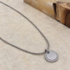 Silver zircon halo round pendant on a snake chain lying on stone
