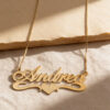 Close up of a 14K yellow gold heart name necklace on a box chain, on beige stone