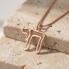 Rose gold open outline Hebrew Chai pendant on a chain, resting on travertine stone