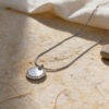 Silver zircon halo pendant on stone in natural sunlight with linen