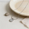 Silver zircon halo necklace beside a stone dish with a pebble