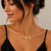 Woman with dark hair in a black top wearing a 14K yellow gold heart name necklace