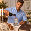 Man pouring red wine into a crystal kiddush cup with saucer at a Friday night Shabbat table with challah and candles
