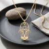 14K yellow gold Hamsa Star of David necklace on a dark stone plate with a pebble