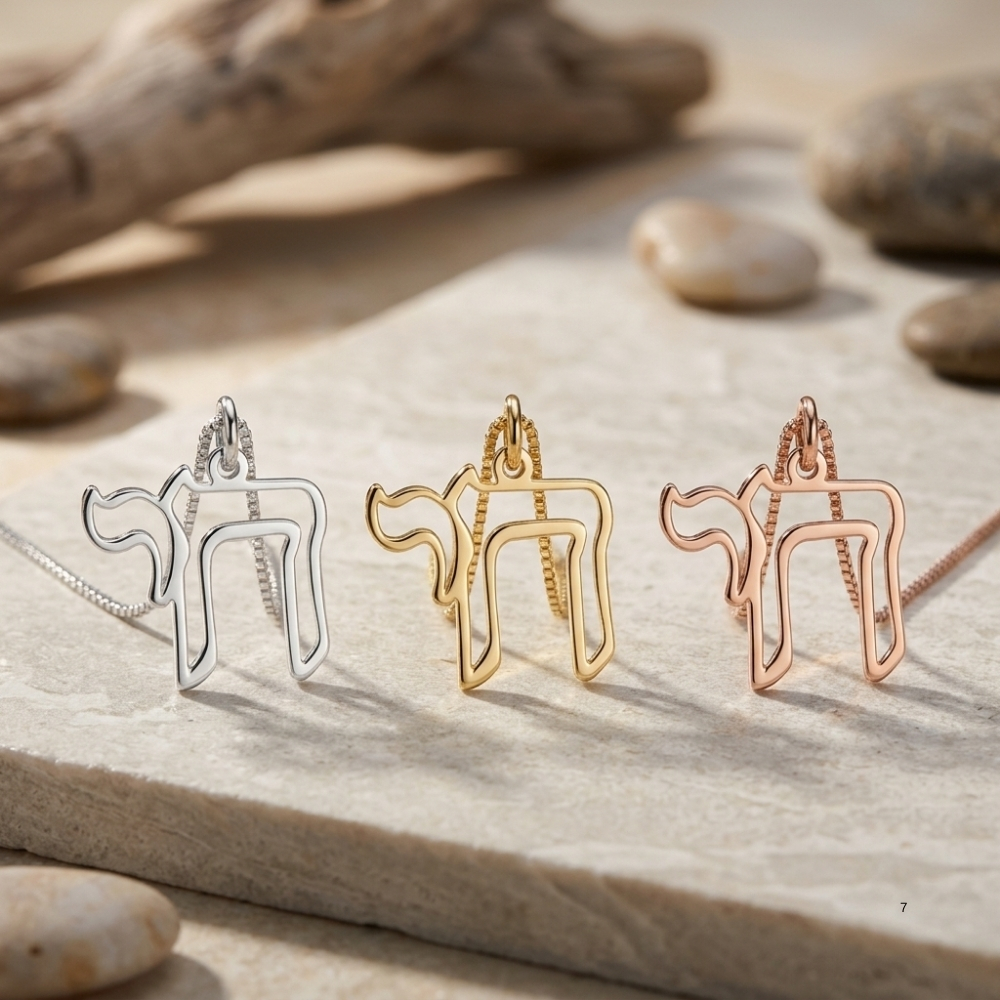 Open outline Hebrew Chai pendants in silver, gold and rose gold displayed on stone