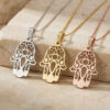 Silver, gold and rose gold Hamsa necklaces with evil eye hanging on a travertine stone block