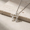 Sterling silver open outline Hebrew Chai pendant resting on light stone